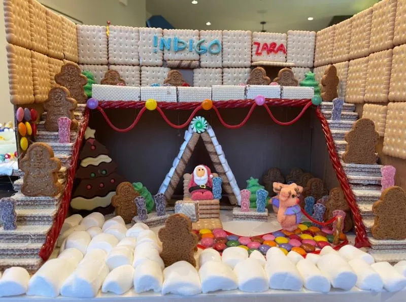 Open-front gingerbread diorama with wafer walls, marshmallow snow and gingerbread people around Santa