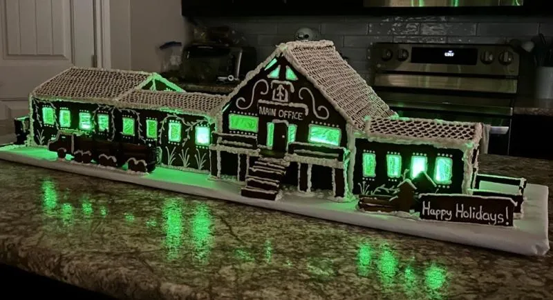 Long gingerbread train station outlined in glowing green lights, reflected on a dark counter