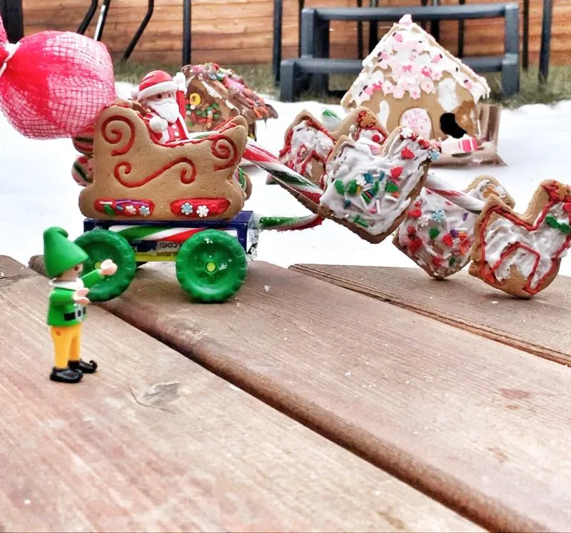 Gingerbread sleigh piled with candy presents, pulled on a green-wheeled cart by a toy elf