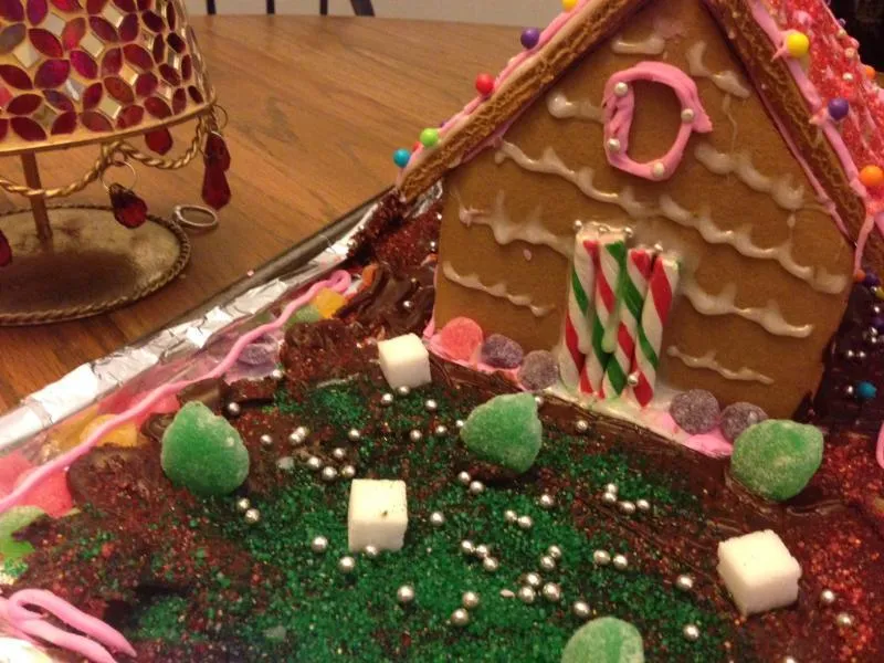 Close-up of a gingerbread house with piped white trim, candy-cane posts and a green sprinkle lawn