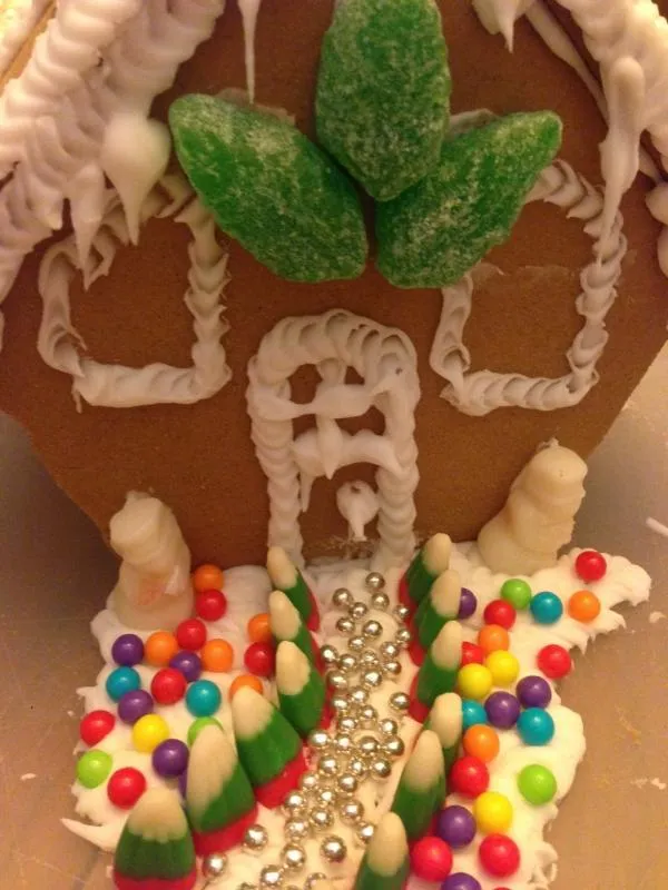Close-up of a gingerbread door with icing swirls, a gumdrop leaf wreath and rainbow candy path