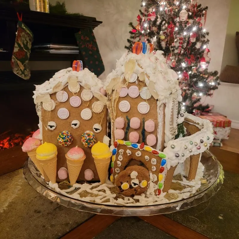 Two gingerbread houses covered in pastel candy buttons and ice-cream cones, beside a lit tree