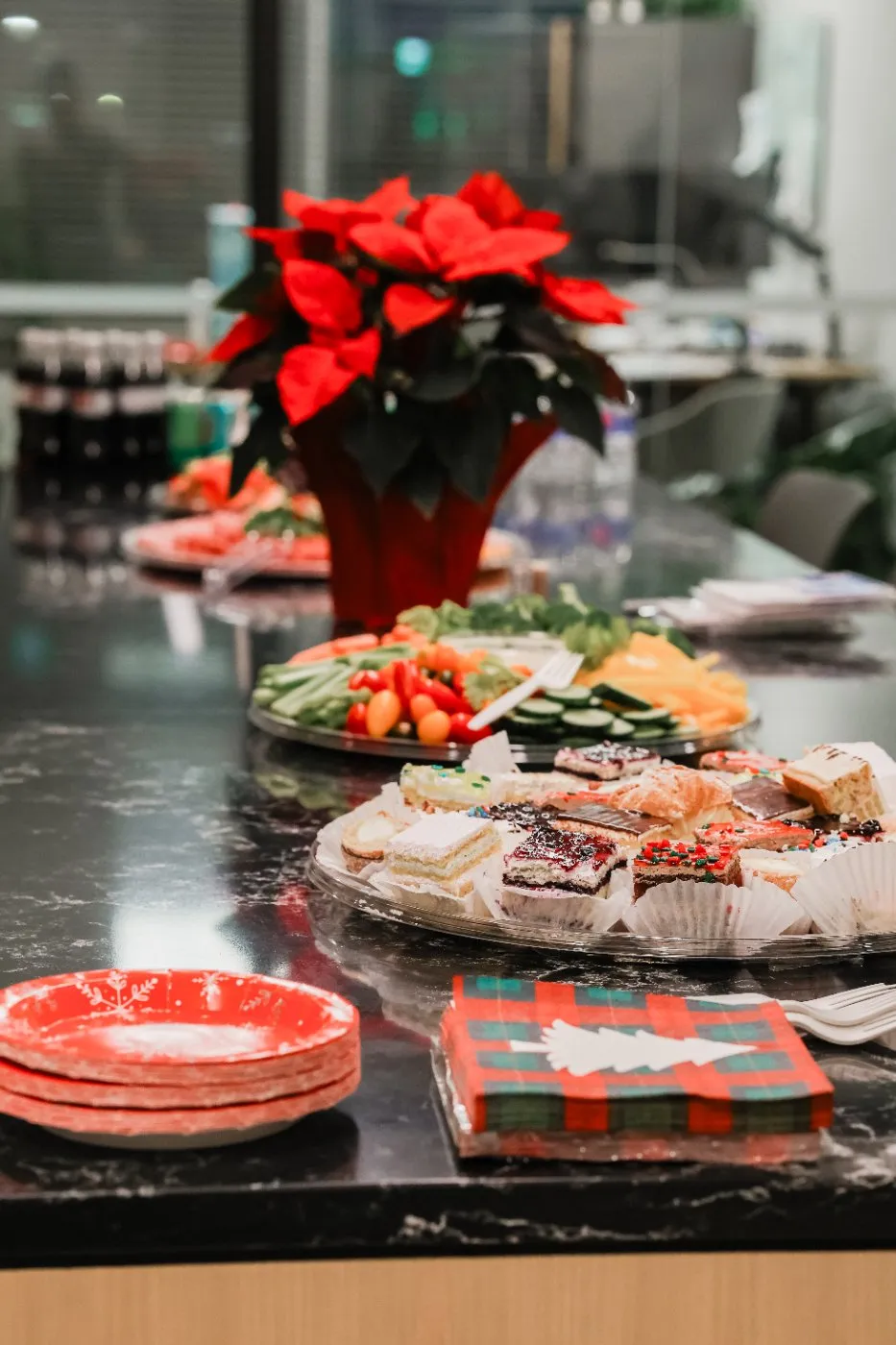 Holiday buffet with a red poinsettia, platters of snacks and stacked red plates