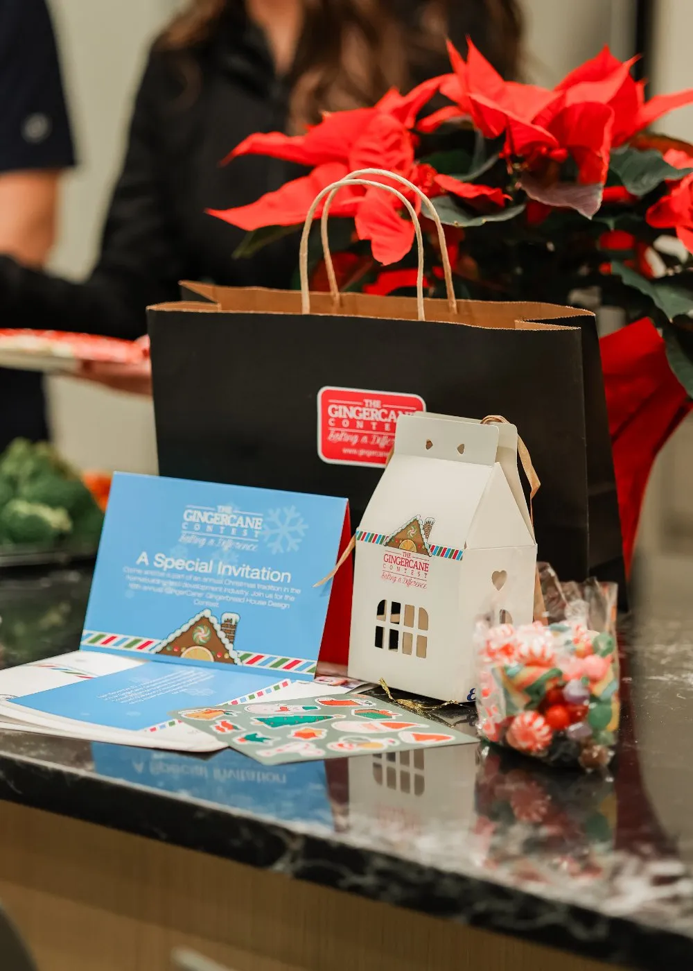 Gift bags, prize baskets and printed GingerCane cards on a counter beside red poinsettias