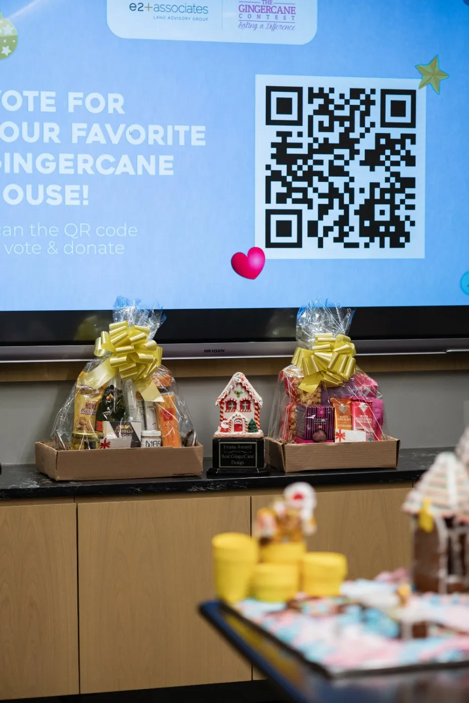 Screen with a QR code to vote for your favourite GingerCane house, above a table of entries